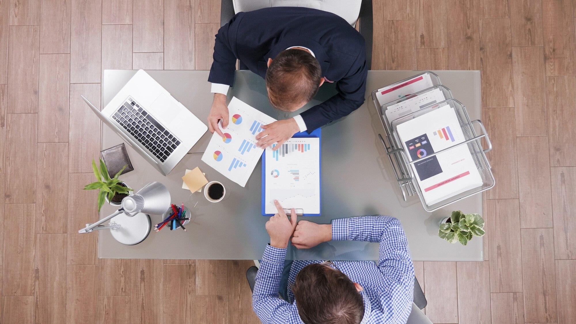 Two colleagues comparing printed workplace charts across a shared desk