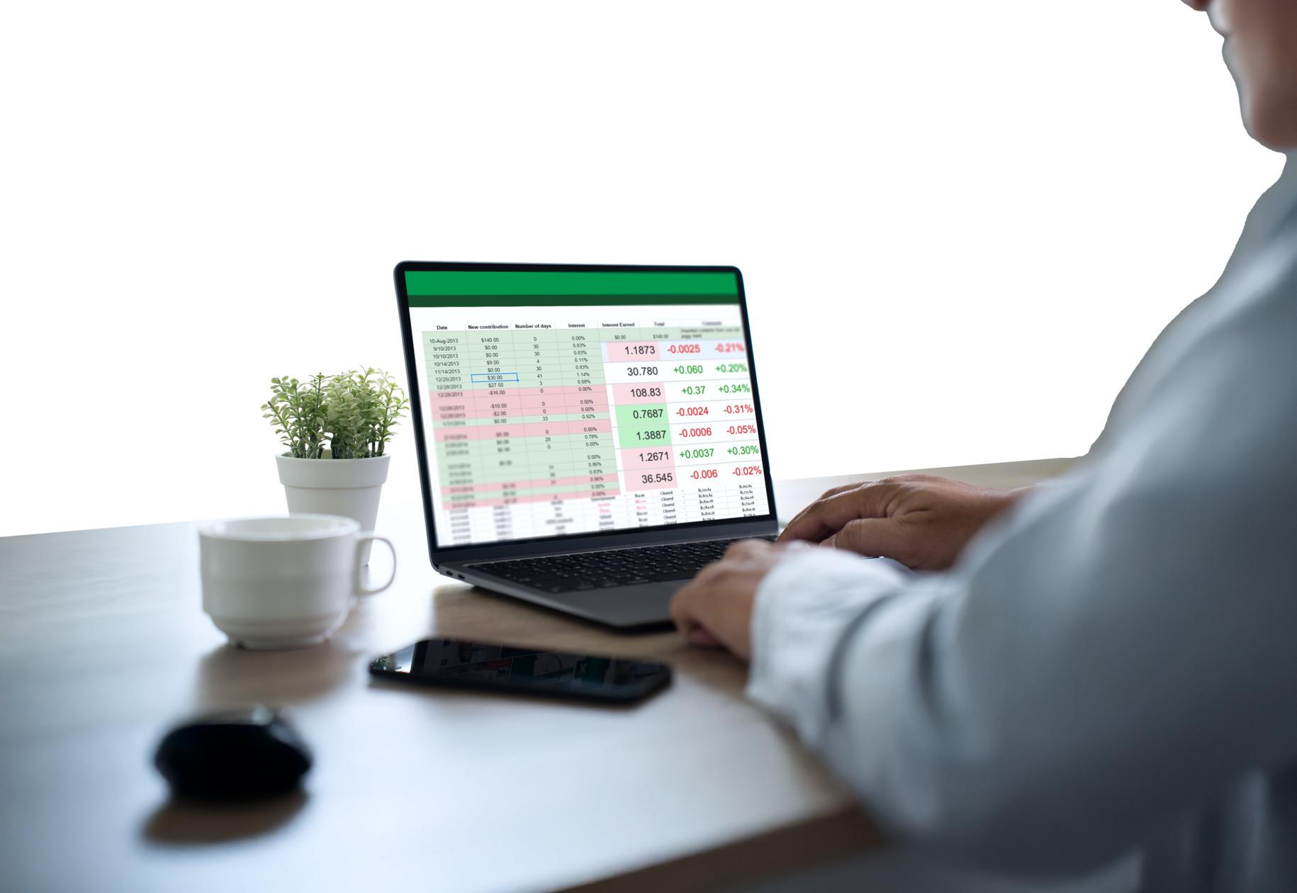 Someone at a desk reading a colour-coded usage report on a laptop, a coffee cup and a small plant beside it