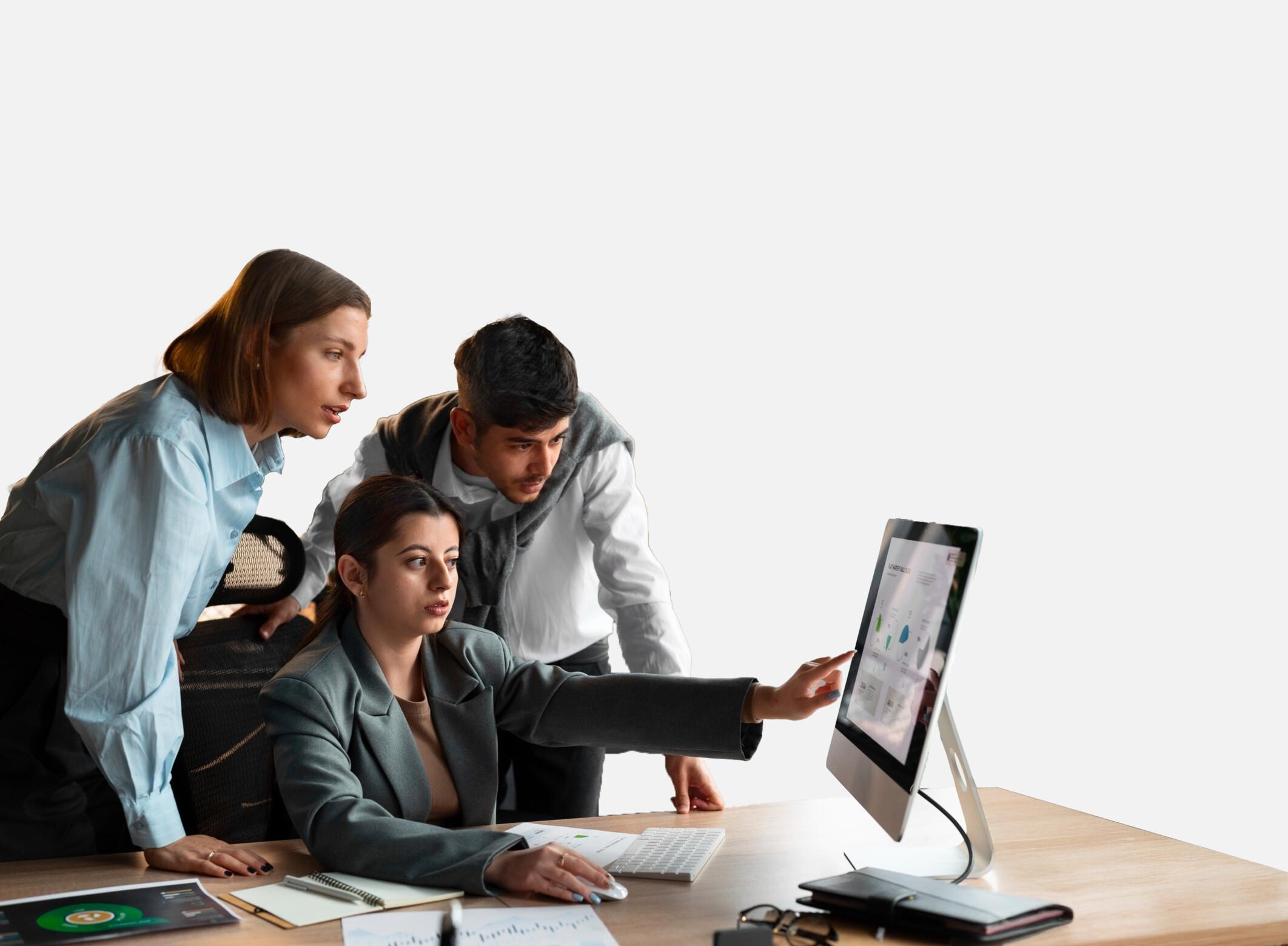 Three colleagues gathered at a desk, one pointing at a workplace dashboard on the monitor